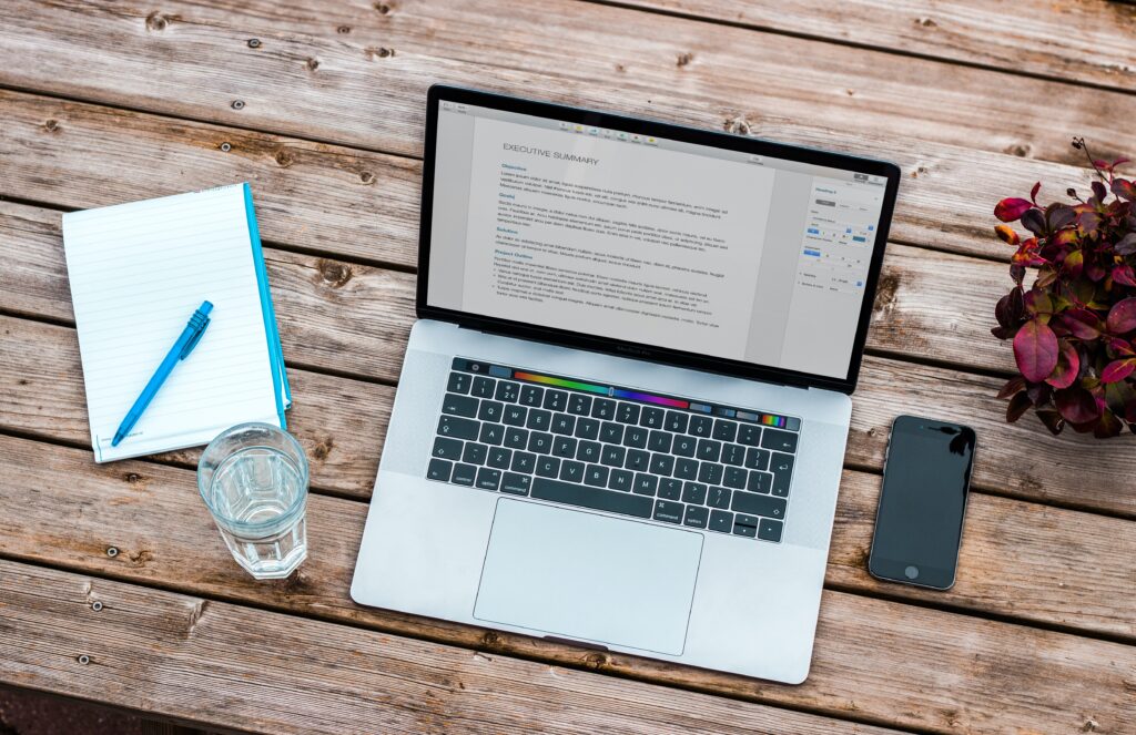 Laptop mit Dokument, Notizblock und Stift auf einem Holztisch – Beitragsbild Lohnadministration