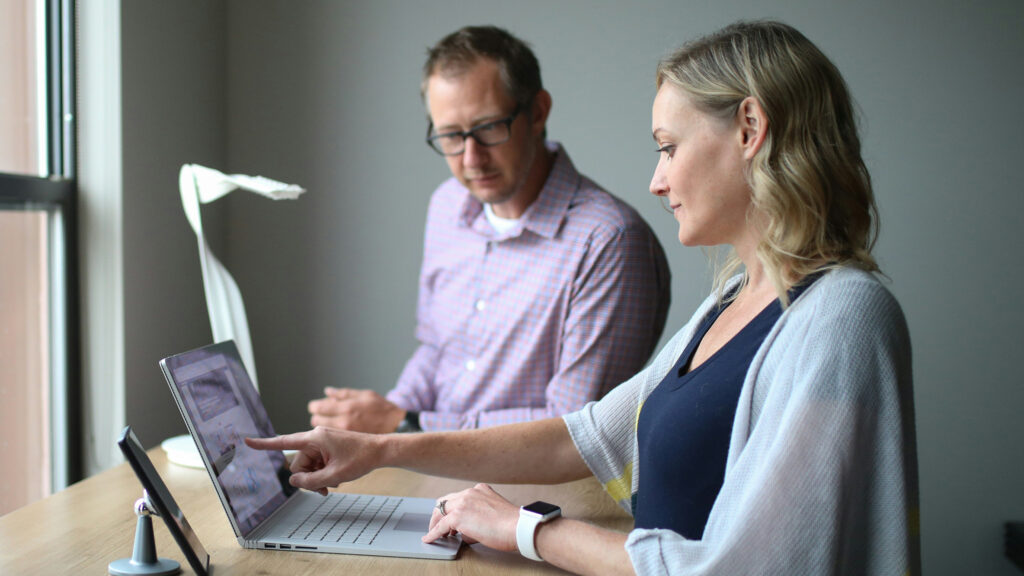 Zwei Personen besprechen gemeinsam Unterlagen an einem Laptop am Fenster